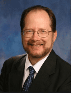 Randall Lord photo portrait; wearing suit & tie & eyeglasses and smiling (color photo)